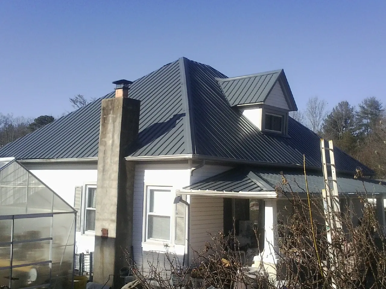 Dark blue standing seam metal roof on a white farmhouse with dormer — Slate & Tile Roof Repair by Roofing Brothers in Bosler