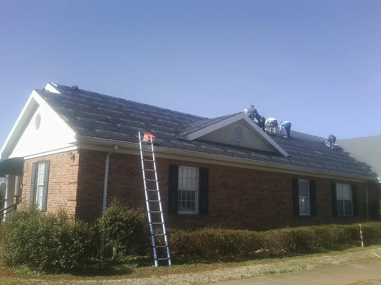Crew tearing shingles off a brick ranch roof with a ladder set — Emergency Roof Repair work by our crew in Bosler