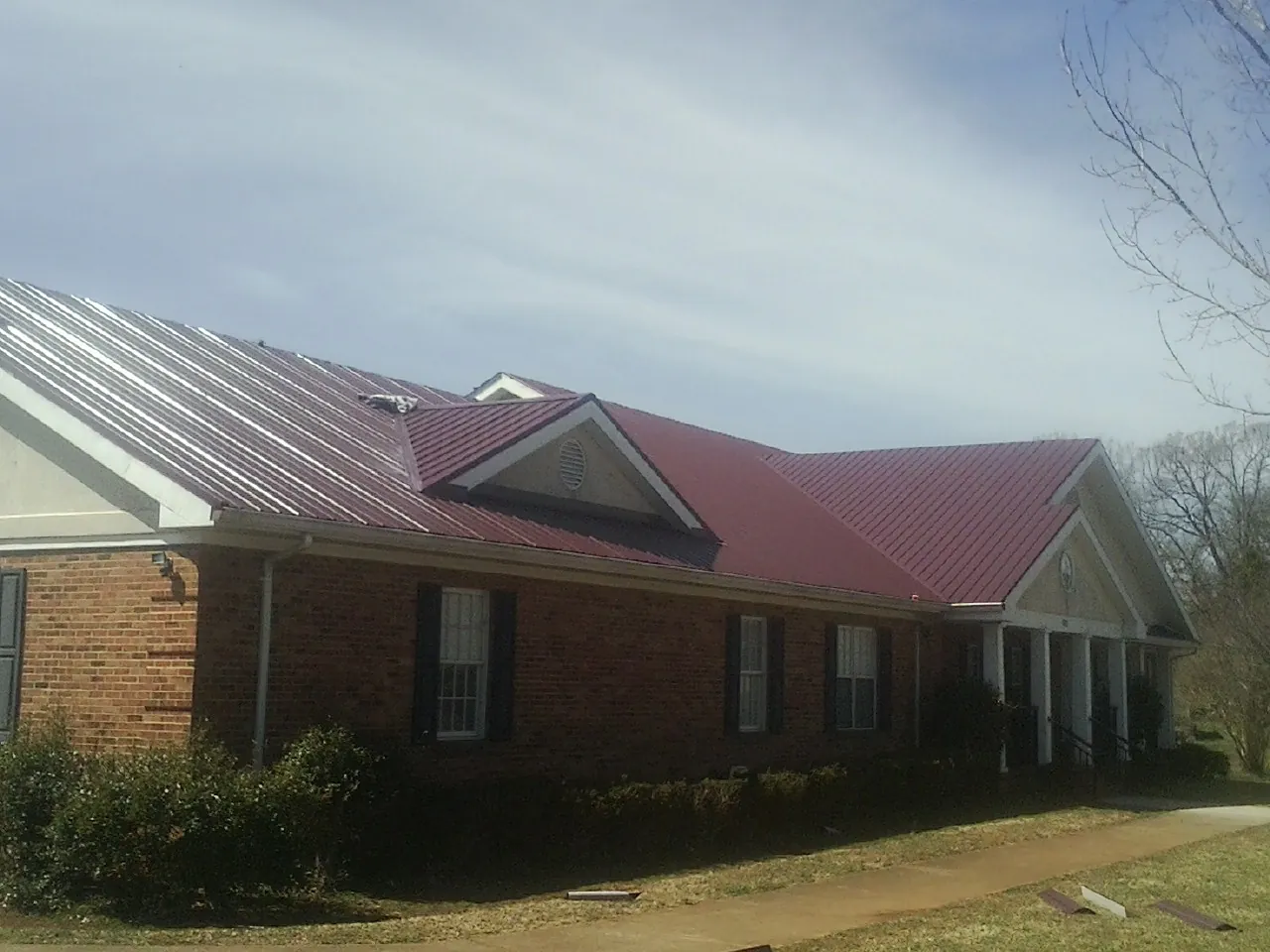 Red metal roof with gabled entries on a long brick building, from a Hail Damage Roof Repair job in Bosler