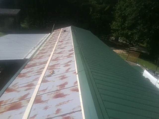 Old rusted panels beside newly installed green metal roofing — Wind Damage Roof Repair by Roofing Brothers in Bosler