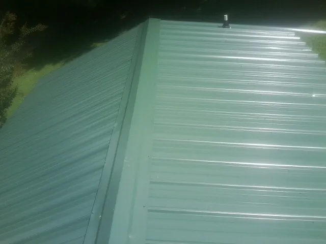 New green metal panels meeting at the ridge of a roof — Flat Roof Repair work by our crew in Bosler