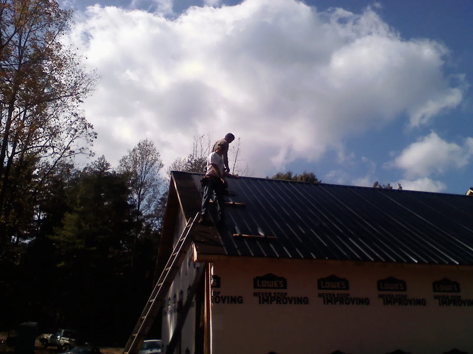 Roofer fastening dark metal panels high against a cloudy sky, from a Roof Inspection job in Bosler