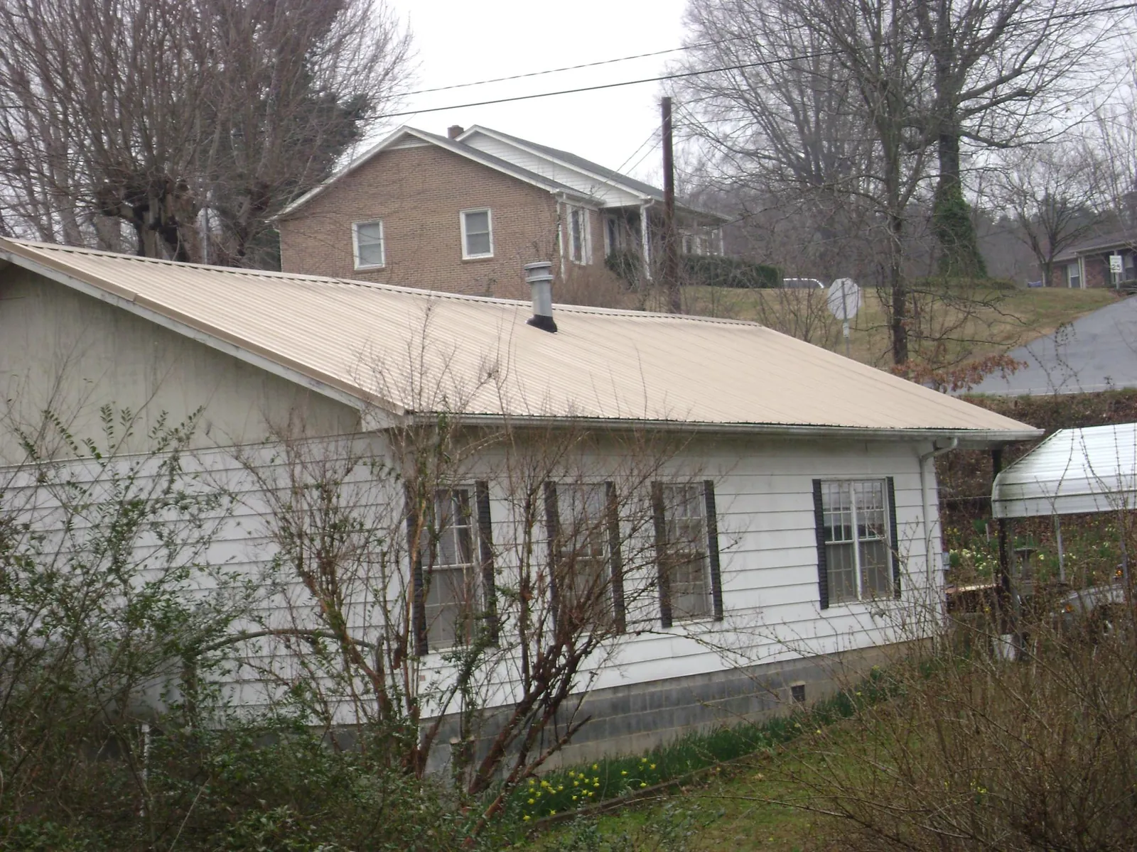 Tan metal roof on a white sided house set into a hillside — Commercial Roofing by Roofing Brothers in Bosler