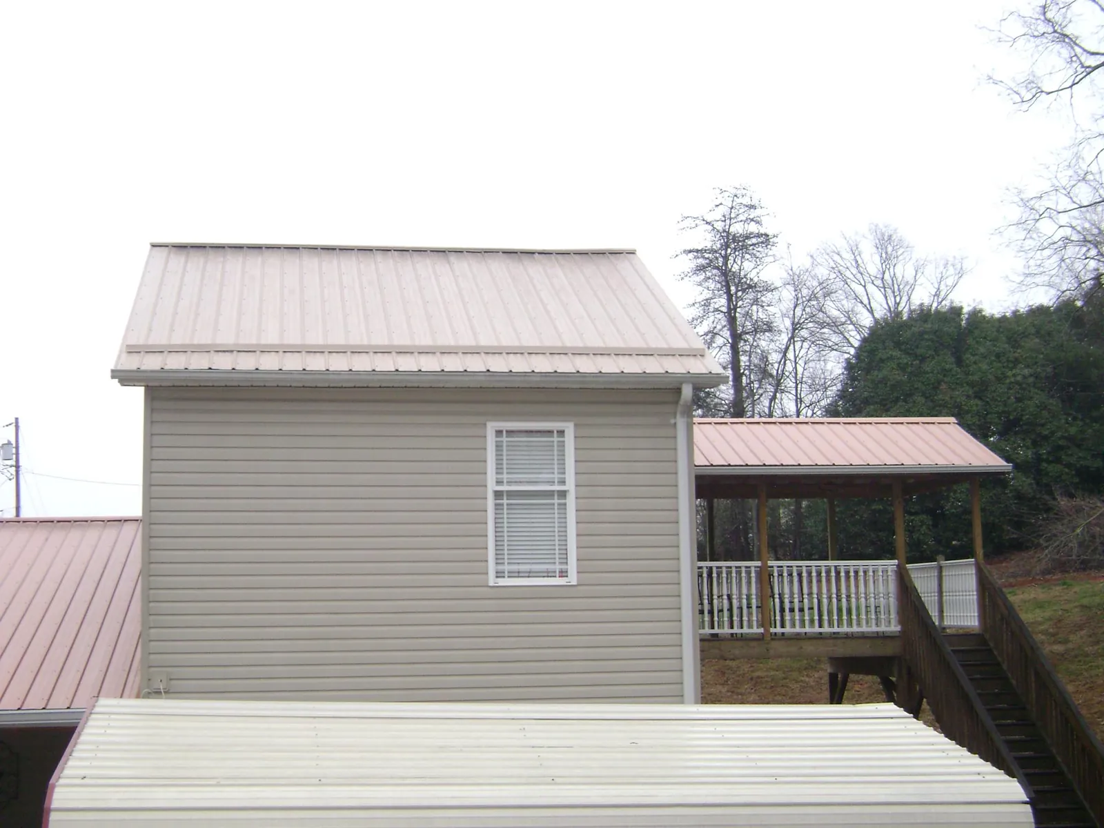 Tan metal roofs on a two story addition and attached porch, from a Roof Replacement job in Bosler